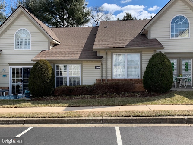 traditional home with a patio area, roof with shingles, uncovered parking, and brick siding