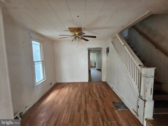 empty room with wood finished floors, a ceiling fan, visible vents, baseboards, and stairway