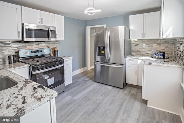 kitchen featuring light stone counters, hanging light fixtures, stainless steel appliances, light wood-style floors, and white cabinetry