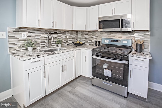 kitchen featuring appliances with stainless steel finishes, white cabinets, a sink, and light wood finished floors