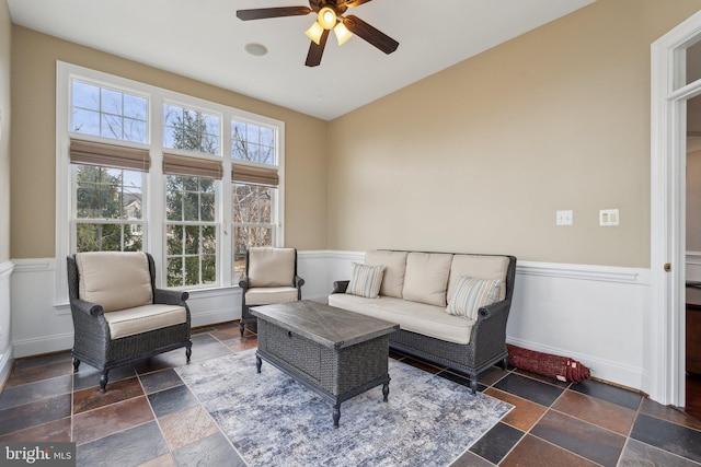 interior space featuring ceiling fan, wainscoting, stone tile flooring, and baseboards