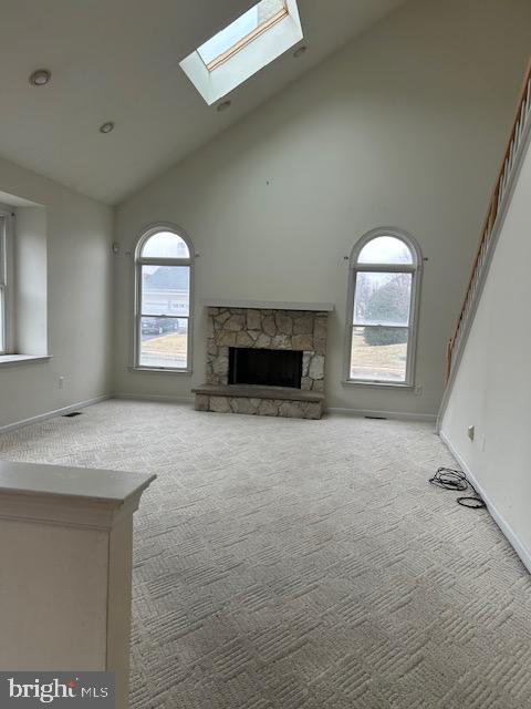 unfurnished living room featuring a skylight, baseboards, carpet flooring, a stone fireplace, and high vaulted ceiling