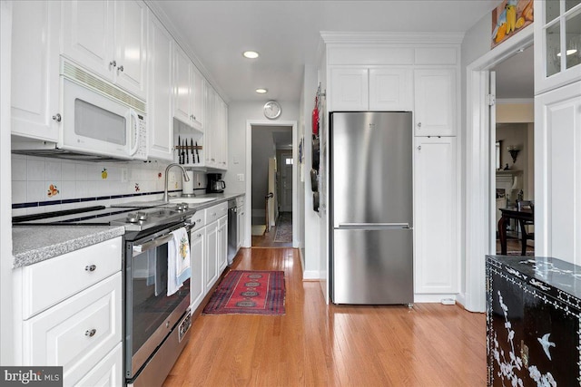 kitchen with light wood finished floors, decorative backsplash, appliances with stainless steel finishes, white cabinets, and a sink