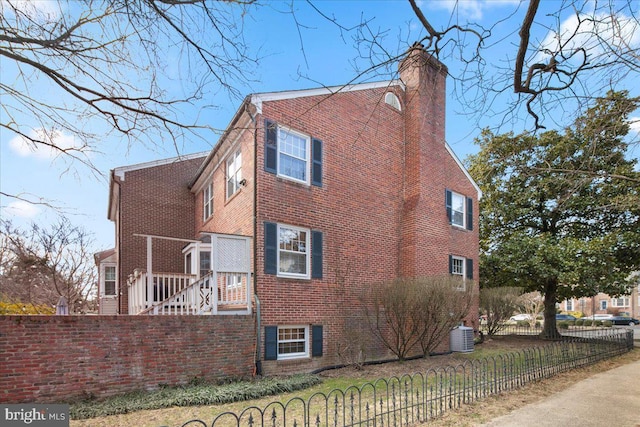 view of property exterior with brick siding, a chimney, fence, and central air condition unit