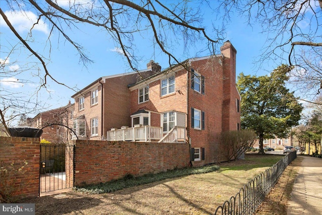 view of home's exterior with a fenced front yard, a gate, brick siding, and a chimney