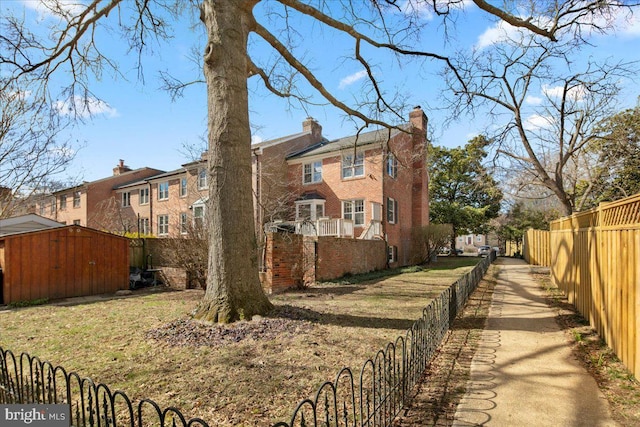 view of home's exterior featuring a chimney, an outbuilding, fence private yard, a shed, and brick siding