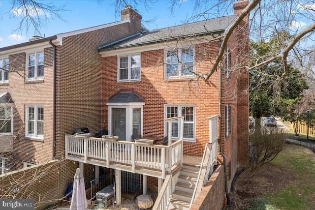 back of house featuring brick siding, a chimney, a wooden deck, and stairway