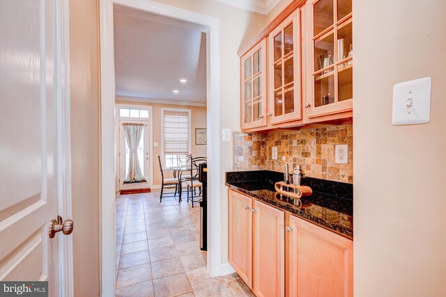 kitchen with ornamental molding, dark stone counters, glass insert cabinets, and tasteful backsplash