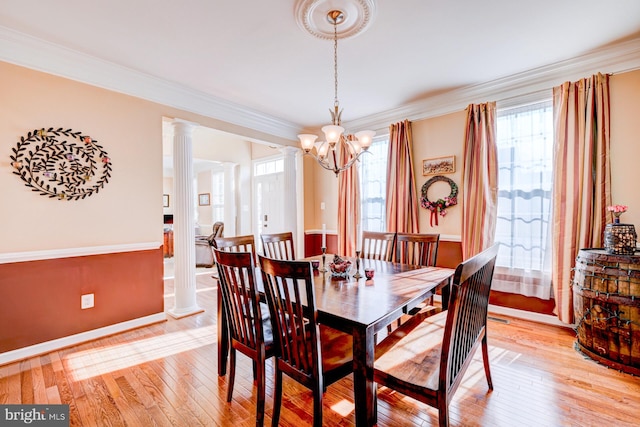 dining area with crown molding, light wood-style floors, a healthy amount of sunlight, and ornate columns