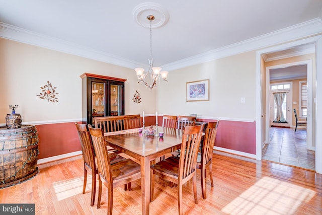 dining room with crown molding, baseboards, light wood-style flooring, and an inviting chandelier