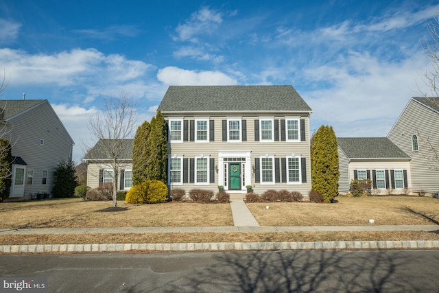 colonial house featuring a shingled roof and a front yard