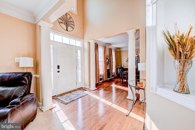 entryway featuring crown molding, a high ceiling, decorative columns, and light wood finished floors