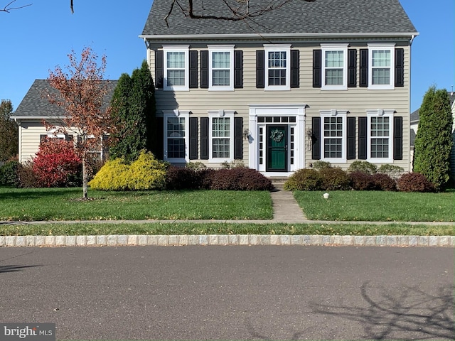 colonial inspired home featuring a front lawn and a shingled roof