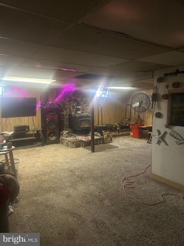 finished basement featuring a wood stove, carpet, and a drop ceiling