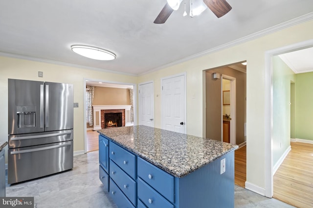 kitchen with blue cabinets, ornamental molding, stainless steel refrigerator with ice dispenser, a kitchen island, and stone counters