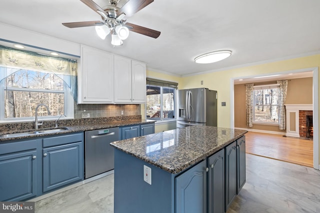 kitchen featuring a kitchen island, ornamental molding, appliances with stainless steel finishes, white cabinetry, and a sink