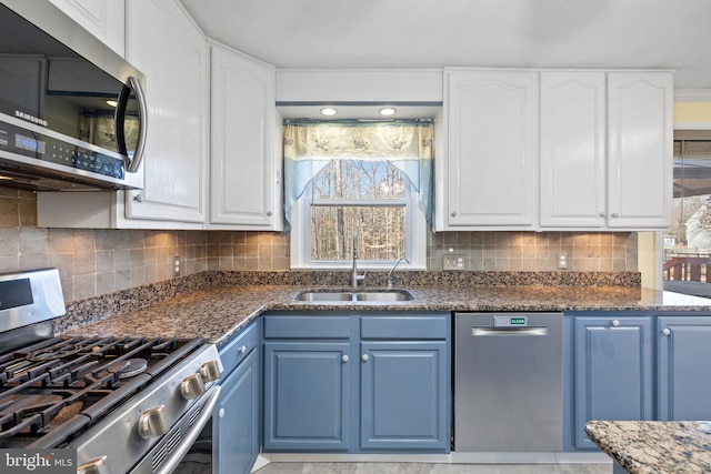 kitchen with a sink, blue cabinetry, tasteful backsplash, stainless steel appliances, and white cabinets