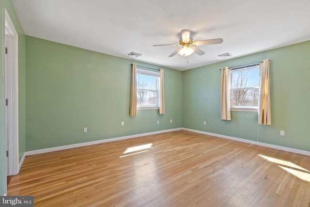 unfurnished room featuring a wealth of natural light, visible vents, light wood-type flooring, and a ceiling fan