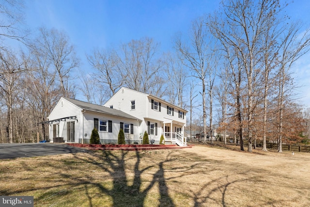 colonial-style house with aphalt driveway, a porch, a front yard, and fence