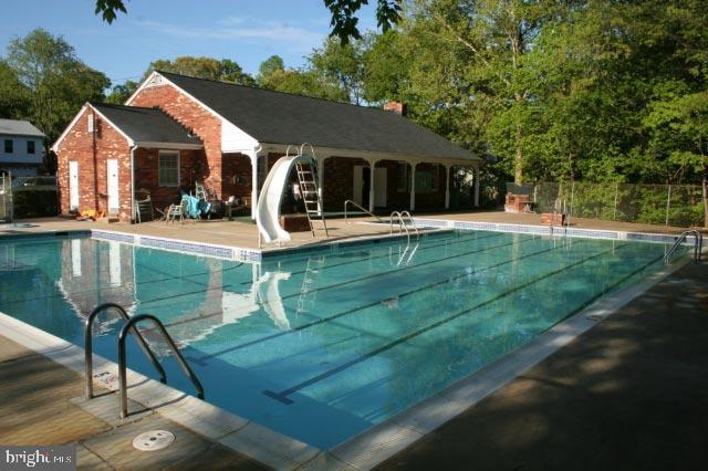 community pool featuring a patio, a water slide, and fence