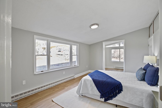 bedroom featuring a baseboard heating unit, multiple windows, and wood finished floors