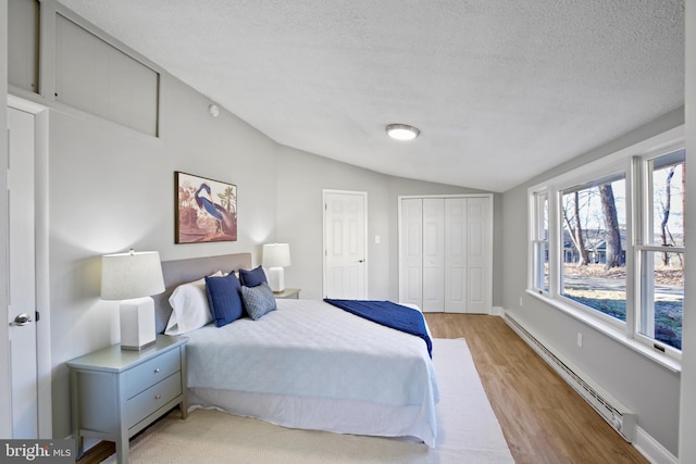 bedroom featuring lofted ceiling, a baseboard heating unit, a textured ceiling, wood finished floors, and baseboards