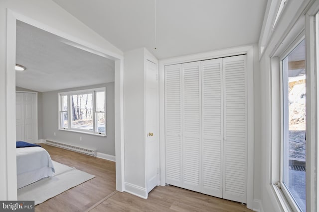 unfurnished bedroom featuring a baseboard radiator, a closet, vaulted ceiling, wood finished floors, and baseboards