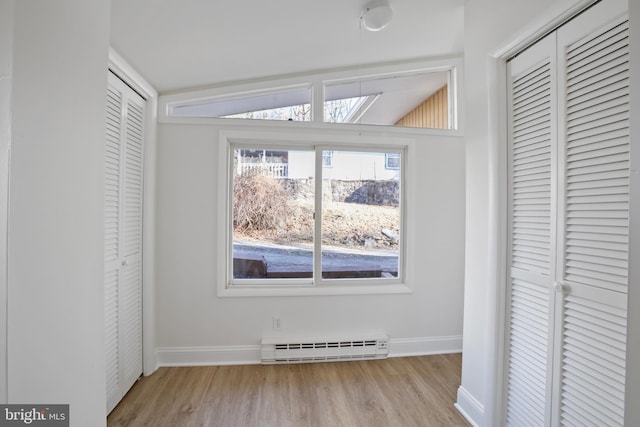 unfurnished bedroom featuring a baseboard heating unit, baseboards, and wood finished floors