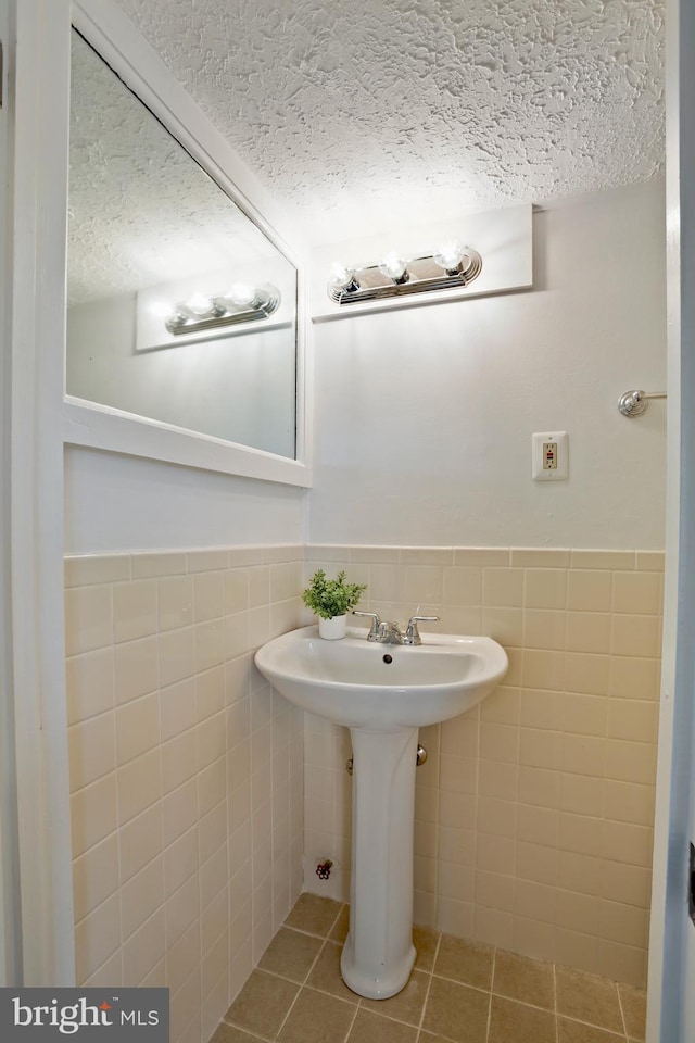 bathroom featuring tile patterned flooring, a wainscoted wall, tile walls, and a textured ceiling