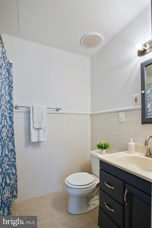 full bath with toilet, a wainscoted wall, tile patterned floors, vanity, and tile walls