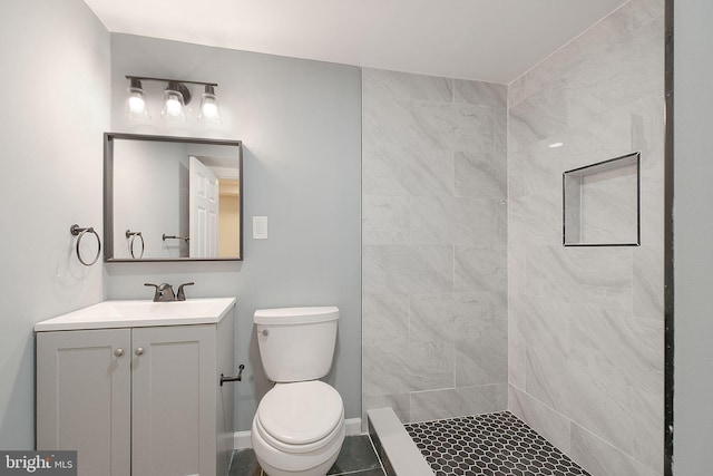 bathroom with tiled shower, vanity, toilet, and baseboards