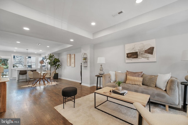 living area featuring recessed lighting, dark wood-type flooring, visible vents, baseboards, and a raised ceiling