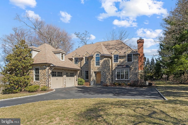 french country inspired facade with aphalt driveway, stone siding, fence, a front yard, and a garage