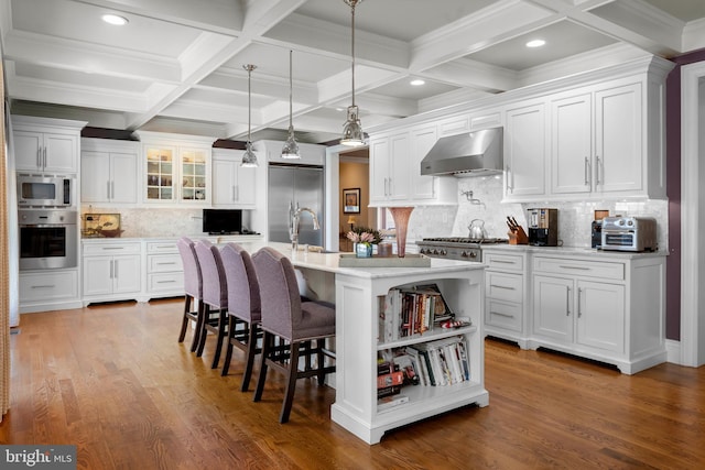 kitchen featuring a breakfast bar, built in appliances, white cabinets, and ventilation hood