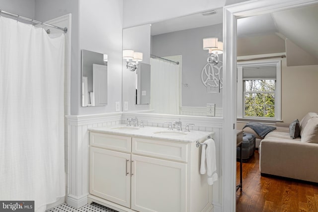 full bathroom featuring double vanity, wood finished floors, lofted ceiling, and a sink