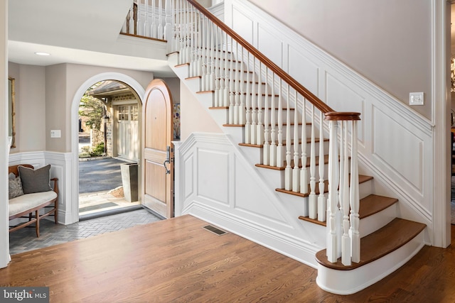 entrance foyer with stairway, a decorative wall, visible vents, and arched walkways