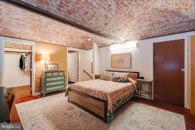 bedroom with dark wood-style floors, brick ceiling, and baseboards