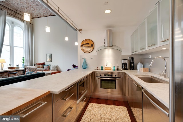 kitchen featuring appliances with stainless steel finishes, glass insert cabinets, a sink, ventilation hood, and light stone countertops