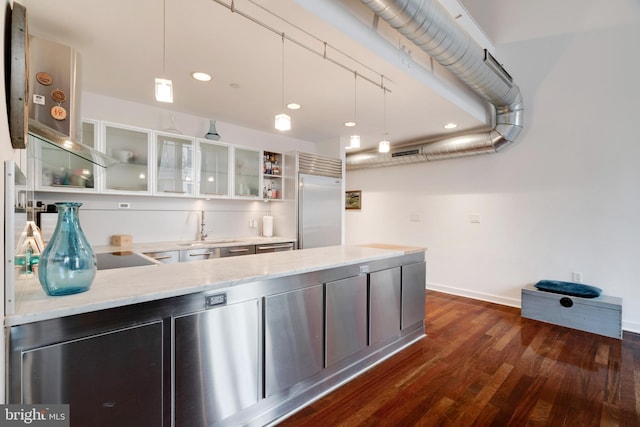 kitchen featuring glass insert cabinets, light stone counters, decorative light fixtures, a sink, and built in fridge