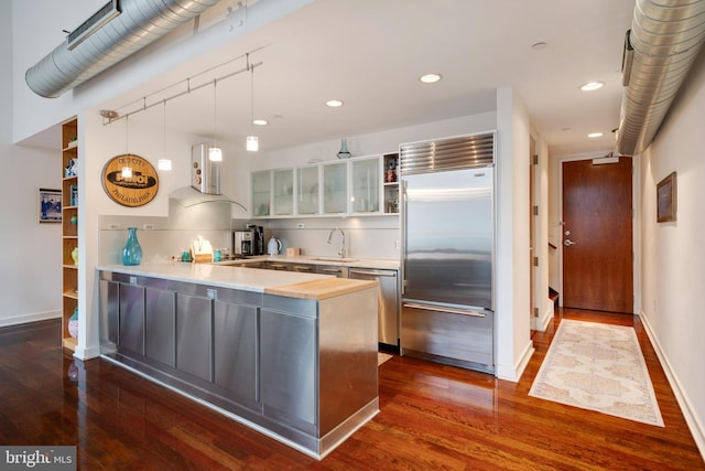 kitchen with dark wood finished floors, glass insert cabinets, extractor fan, stainless steel appliances, and light countertops