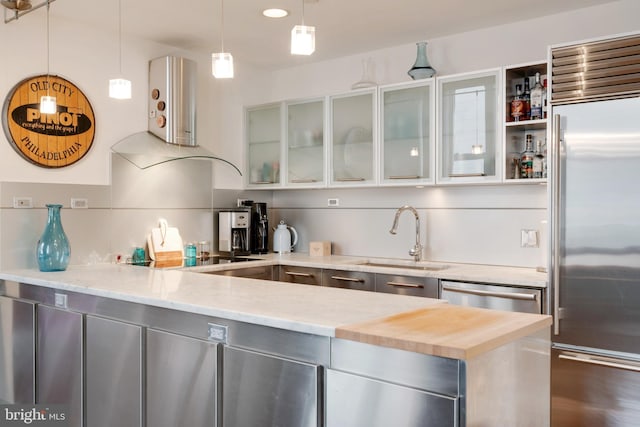 kitchen featuring stainless steel appliances, a sink, hanging light fixtures, light stone countertops, and glass insert cabinets