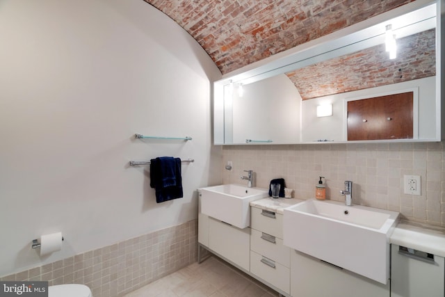 full bathroom featuring double vanity, brick ceiling, a sink, and lofted ceiling