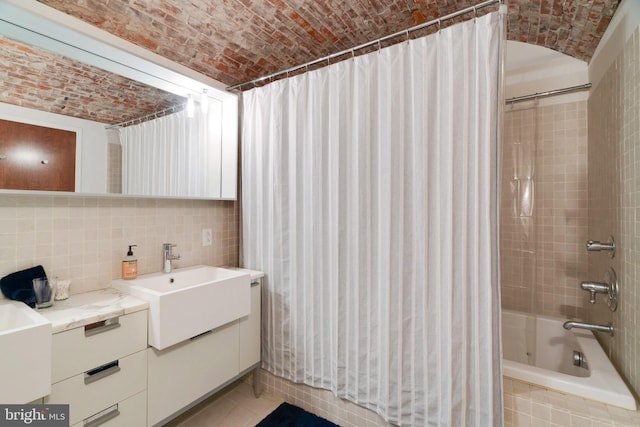 full bathroom featuring tasteful backsplash, brick ceiling, tiled shower / bath, vanity, and tile walls