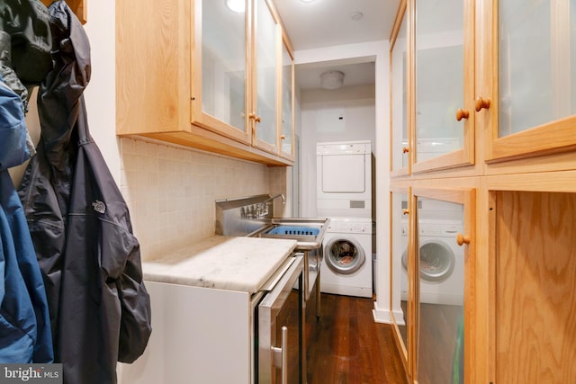 clothes washing area with dark wood-style floors, laundry area, a sink, and stacked washing maching and dryer