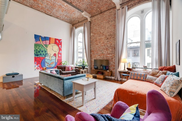 living area with brick ceiling, a towering ceiling, baseboards, and wood finished floors