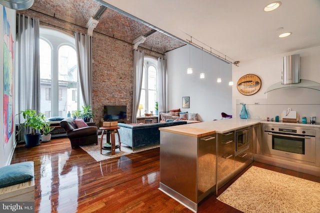 kitchen featuring dark wood-style floors, appliances with stainless steel finishes, open floor plan, a peninsula, and exhaust hood