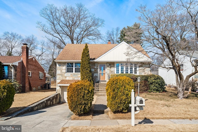 view of front facade with driveway, stone siding, a shingled roof, and a chimney