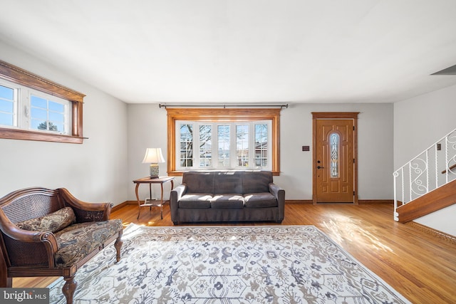 living area with light wood-style floors, stairs, baseboards, and a wealth of natural light