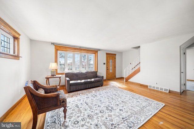 living room featuring visible vents, light wood-style flooring, baseboards, and stairs