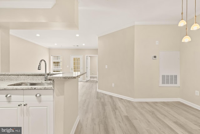 kitchen featuring crown molding, hanging light fixtures, light wood-style floors, a sink, and baseboards